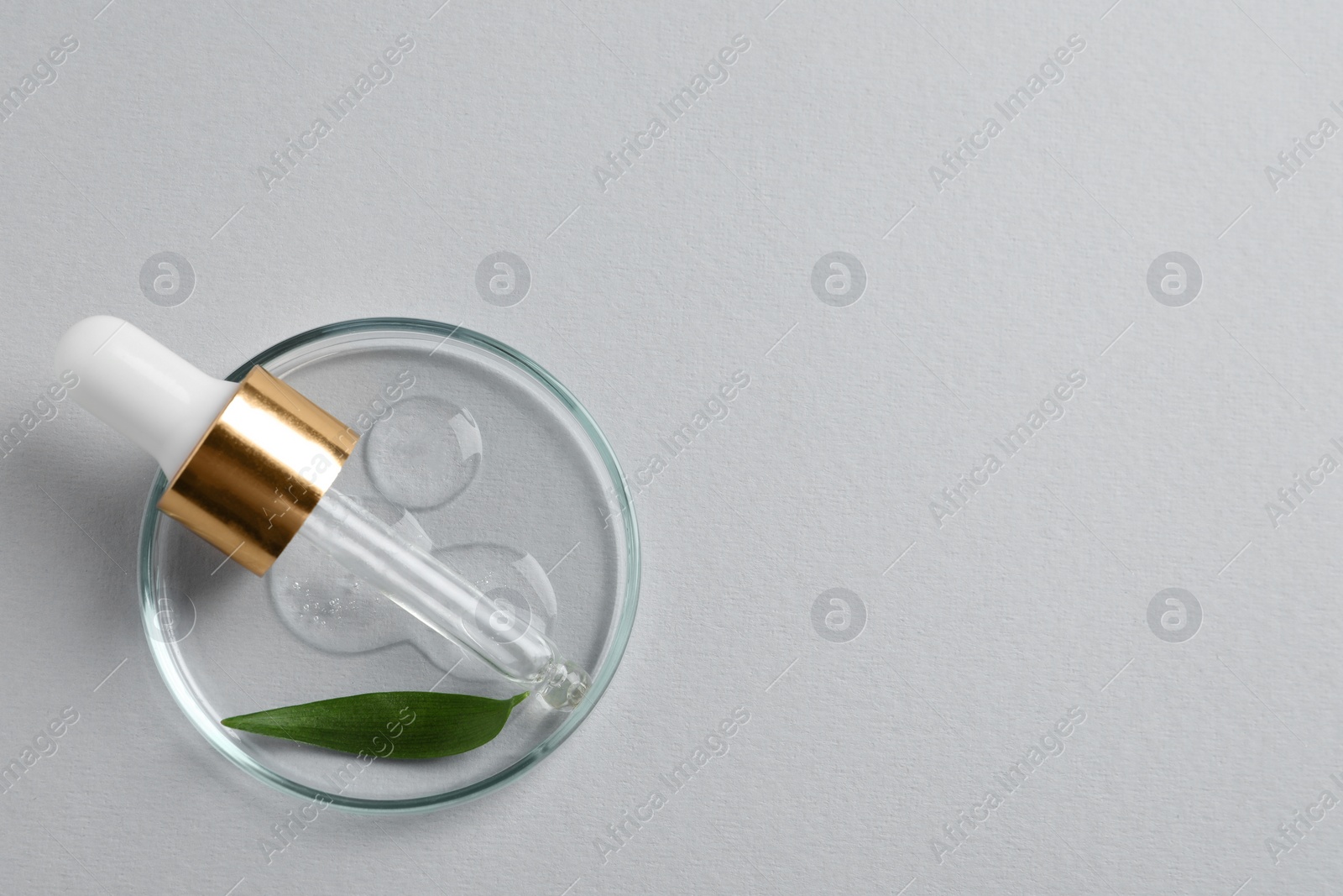 Photo of Petri dish with sample of cosmetic oil, pipette and green leaf on white background, top view. Space for text