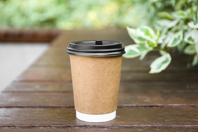 Photo of Paper cup on wooden bench outdoors. Takeaway drink