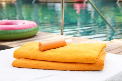 Photo of Beach towels and sunscreen on sun lounger near outdoor swimming pool, selective focus. Luxury resort