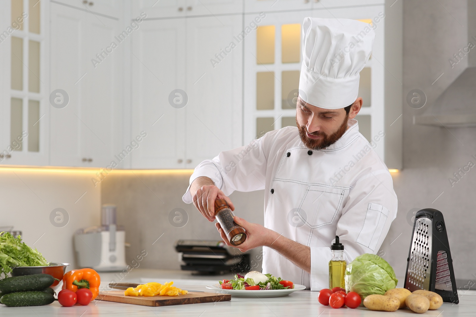 Photo of Professional chef adding pepper into delicious salad at marble table in kitchen