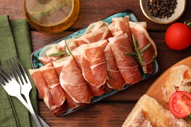 Photo of Rolled slices of delicious jamon served with different products on wooden table, flat lay