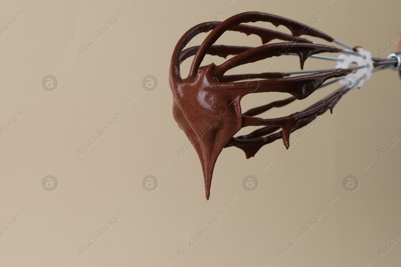 Photo of Chocolate cream flowing from whisk on beige background, closeup. Space for text