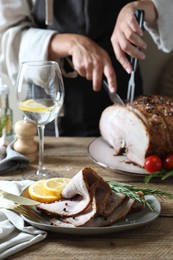 Woman cutting delicious baked ham at wooden table, selective focus