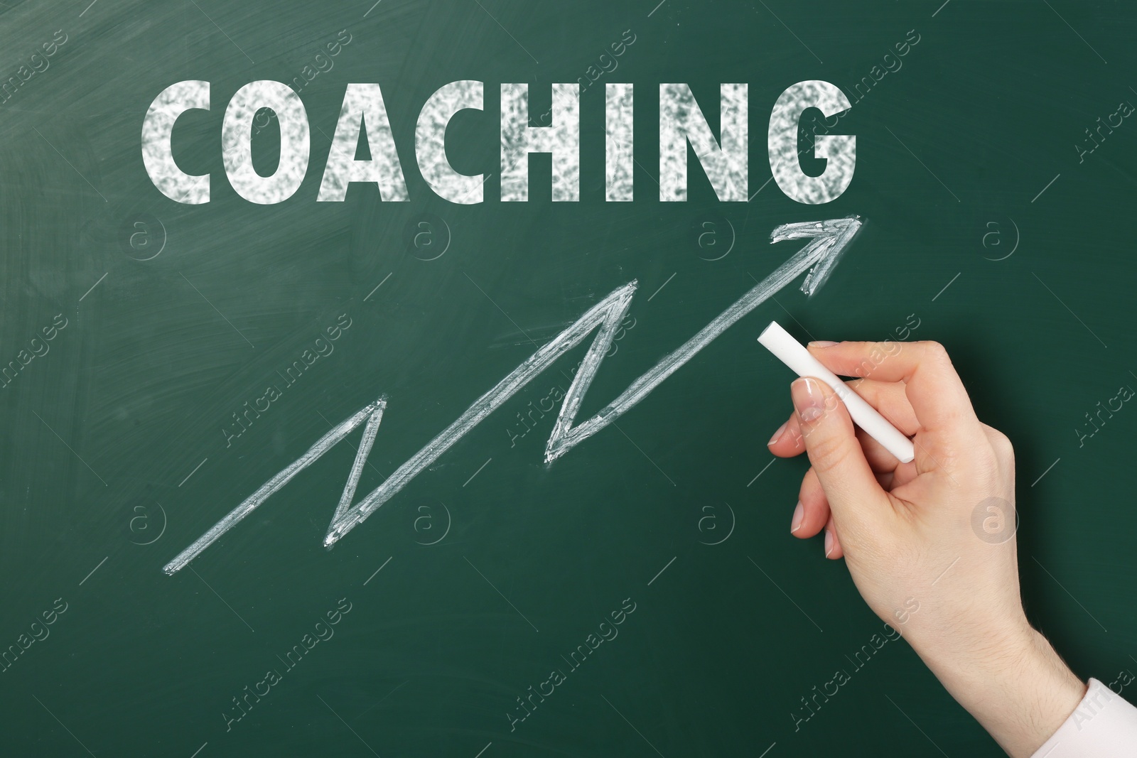 Image of Business or life trainer drawing arrow under word Coaching on green chalkboard, closeup