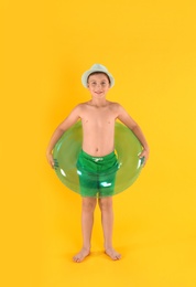 Photo of Cute little child in beachwear with bright inflatable ring on yellow background