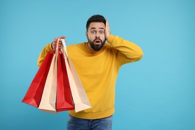 Photo of Shocked man with many paper shopping bags on light blue background. Space for text
