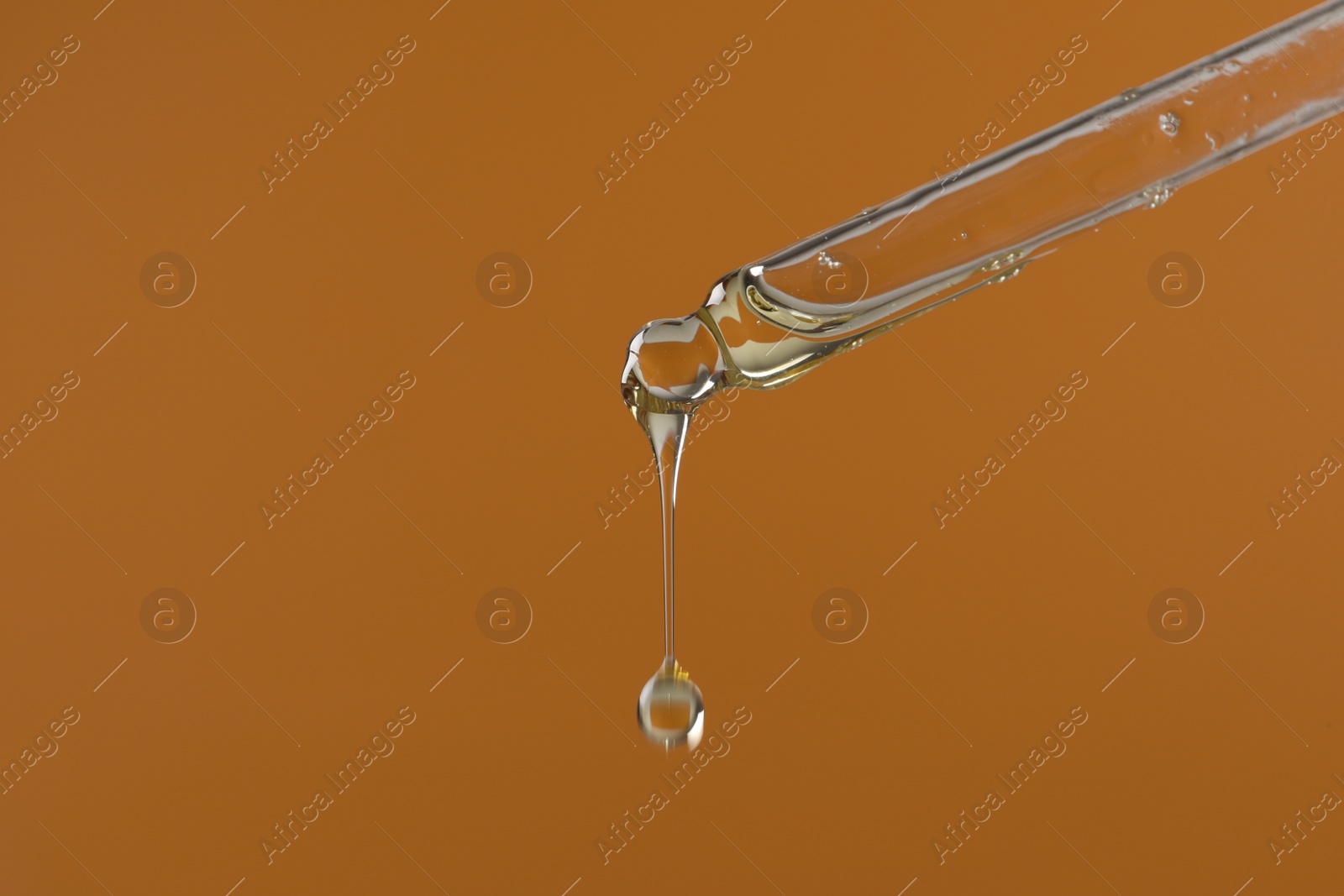 Photo of Dripping hydrophilic oil from pipette on brown background, closeup. Space for text