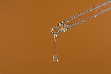 Photo of Dripping hydrophilic oil from pipette on brown background, closeup. Space for text