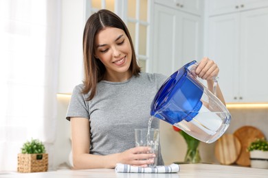 Woman pouring water from filter jug into glass in kitchen