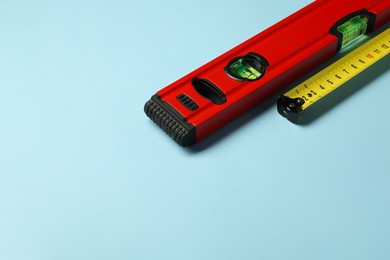 Photo of Building level and tape measure on light blue background. Space for text