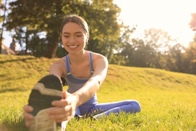 Photo of Attractive woman doing exercises on green grass in park, space for text. Stretching outdoors