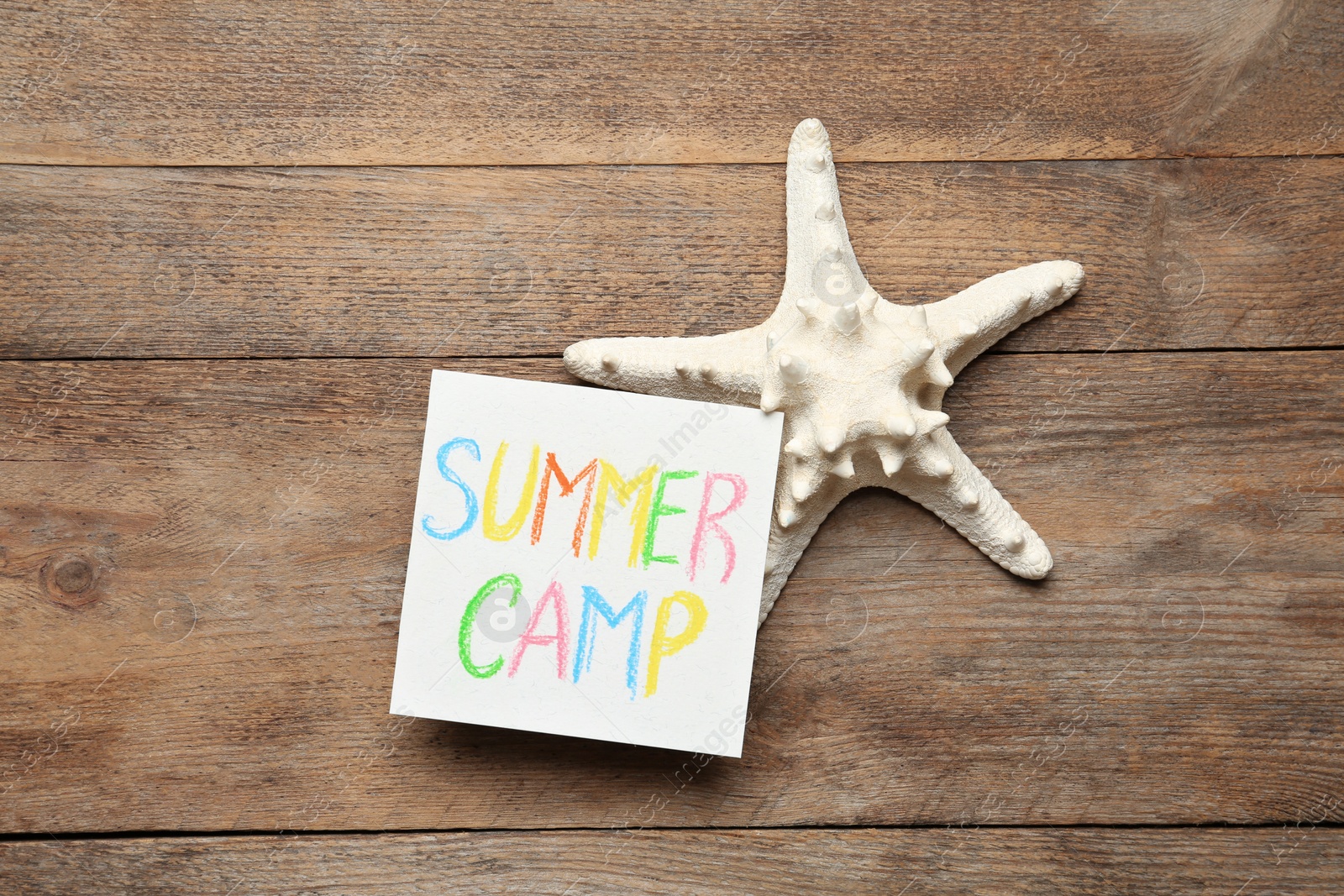 Photo of Card with text SUMMER CAMP and starfish on wooden table, flat lay