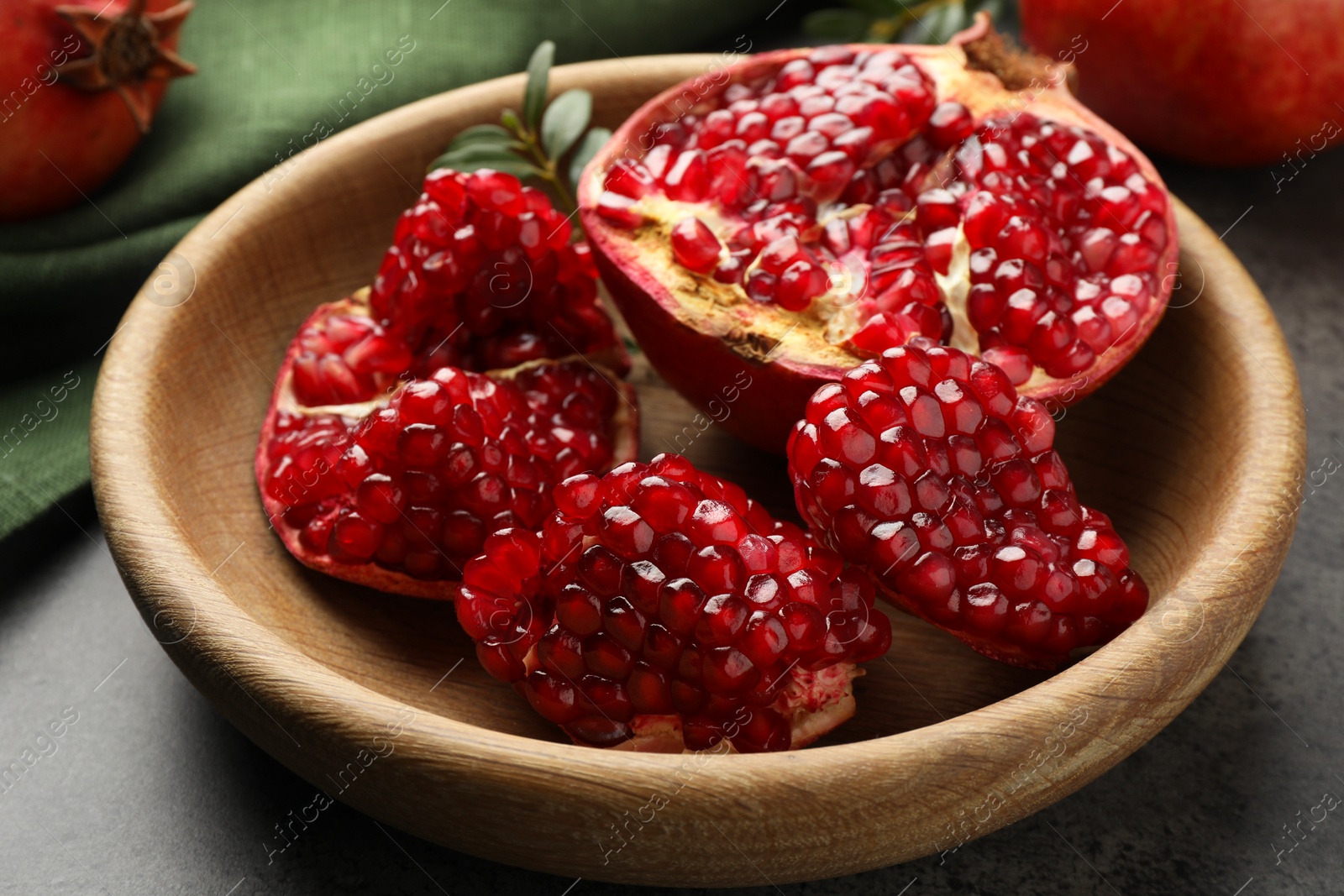 Photo of Cut fresh pomegranate in bowl on grey table, closeup