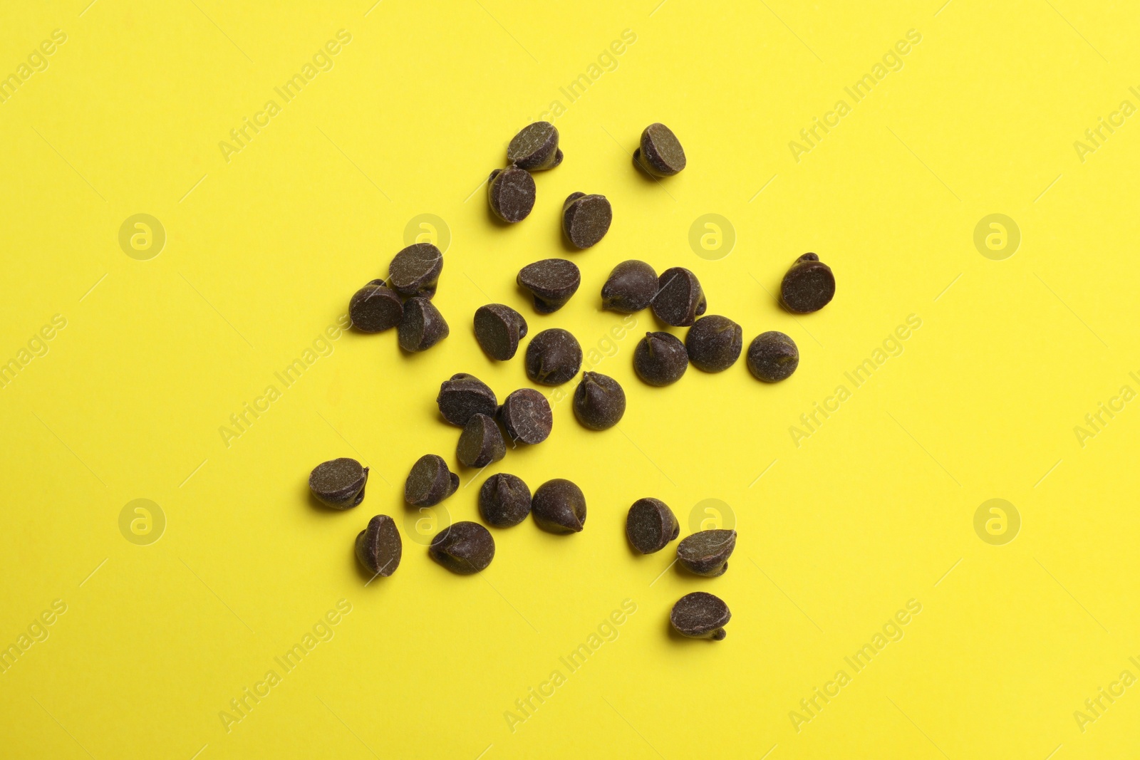 Photo of Delicious chocolate chips on yellow background, top view