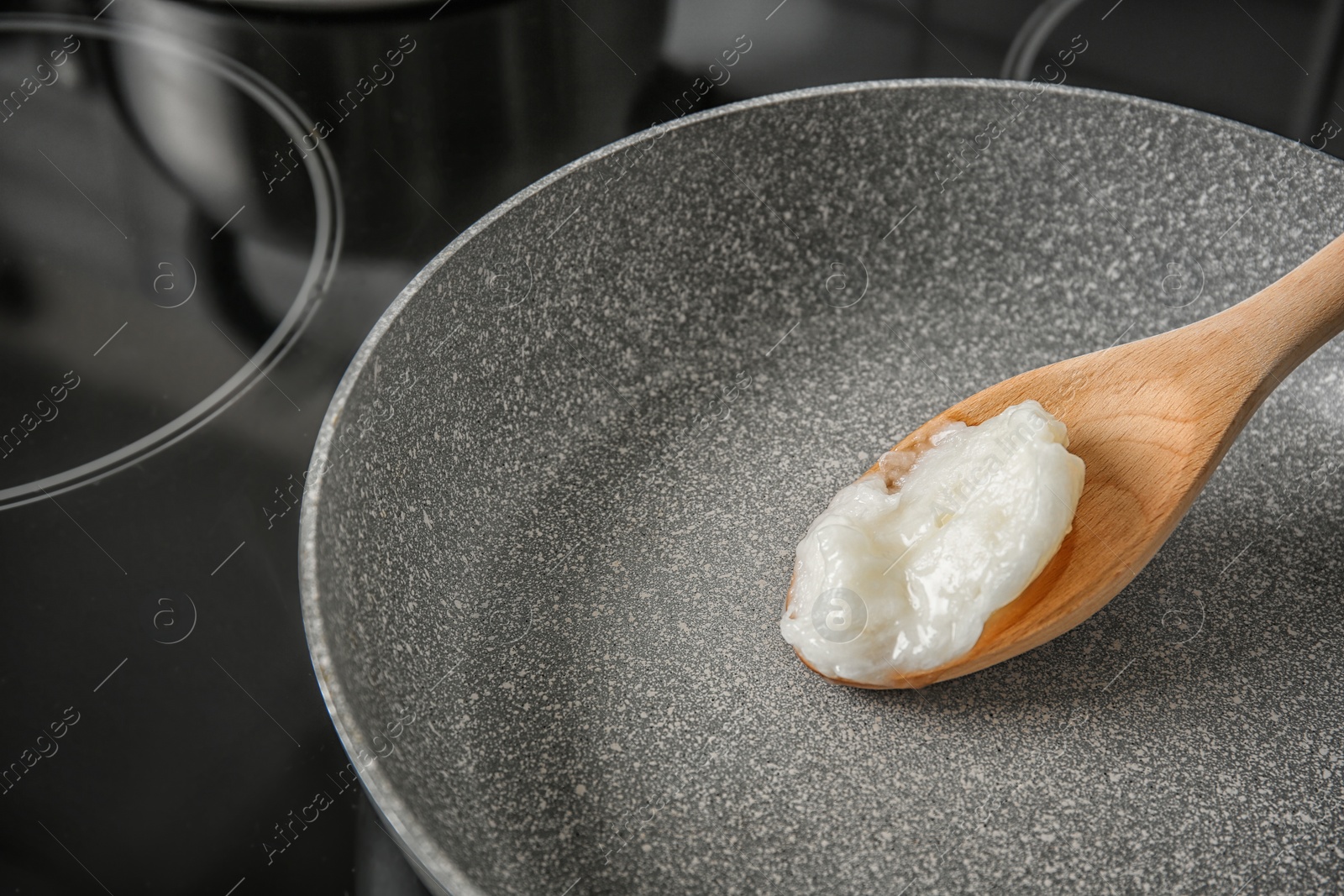 Photo of Wooden spoon with coconut oil in frying pan. Healthy cooking