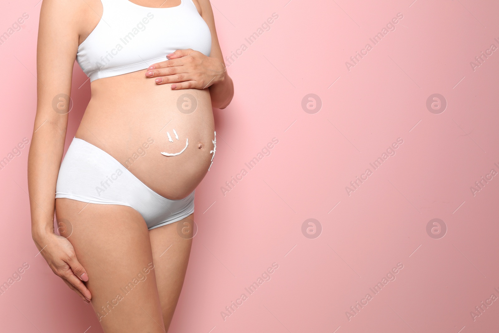 Photo of Smile painted with body cream on pregnant woman's belly against color background, closeup. Space for text