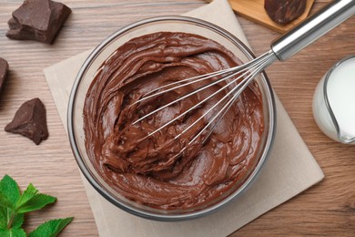 Photo of Whipping chocolate cream with balloon whisk on wooden table, flat lay