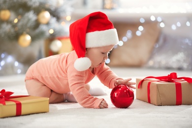 Little baby in Santa hat with Christmas decoration on floor at home