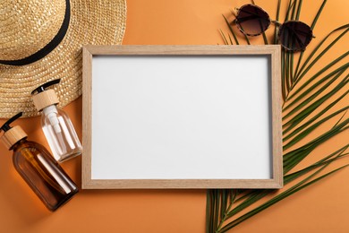 Photo of Blank photo frame, straw hat, cosmetics, sunglasses and tropical leaf on orange background, flat lay