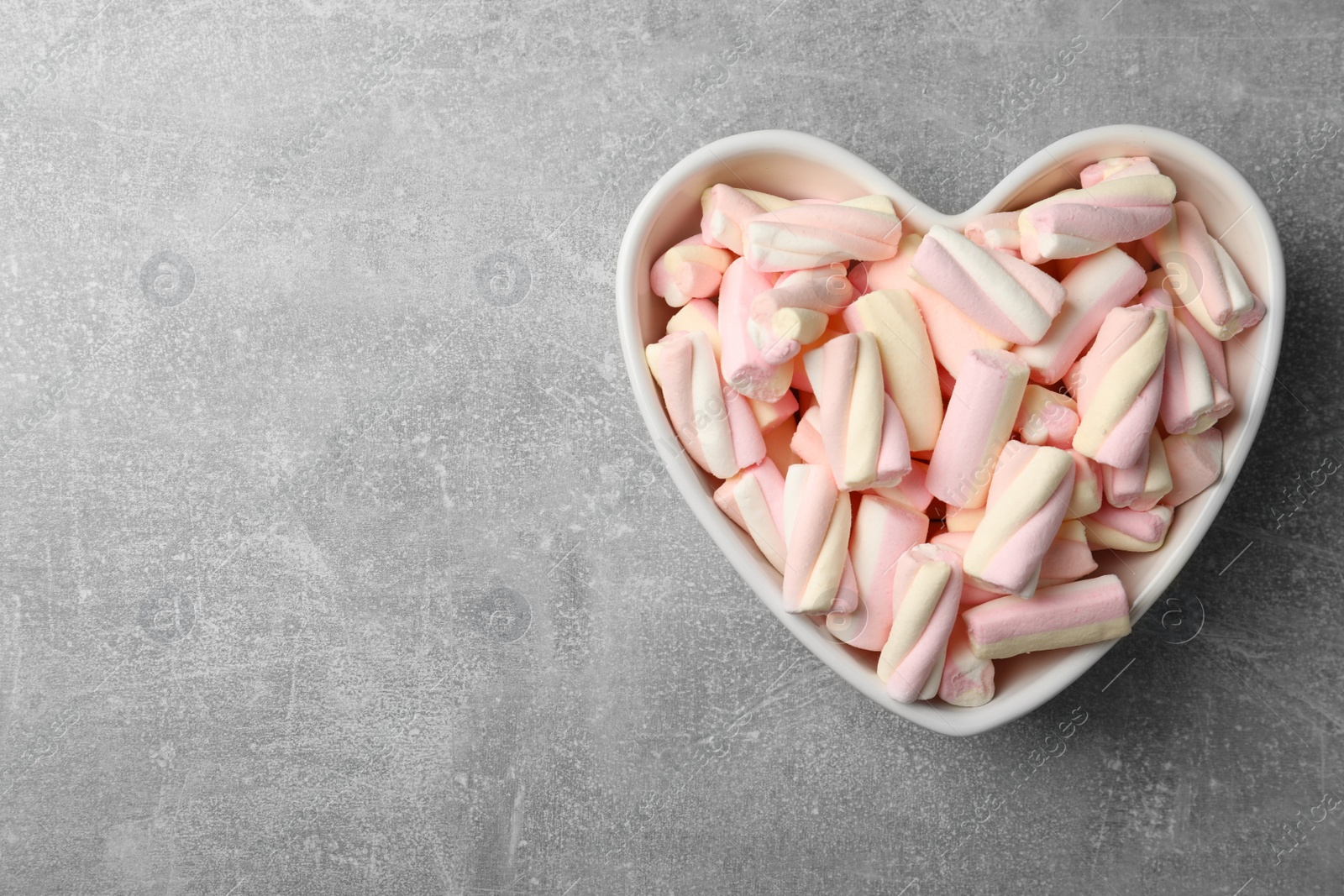 Photo of Marshmallows in heart shaped bowl on grey table, top view. Space for text