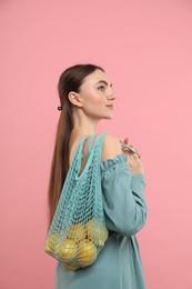 Photo of Woman with string bag of fresh lemons on pink background