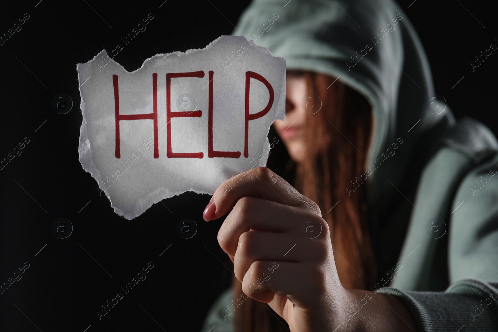 Photo of Woman holding piece of paper with word Help on black background, closeup. Domestic violence concept