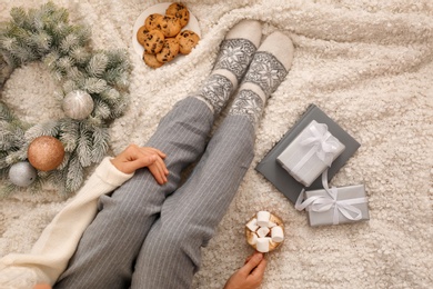 Photo of Young woman with cocoa and cookies sitting on light blanket, top view. Christmas holiday