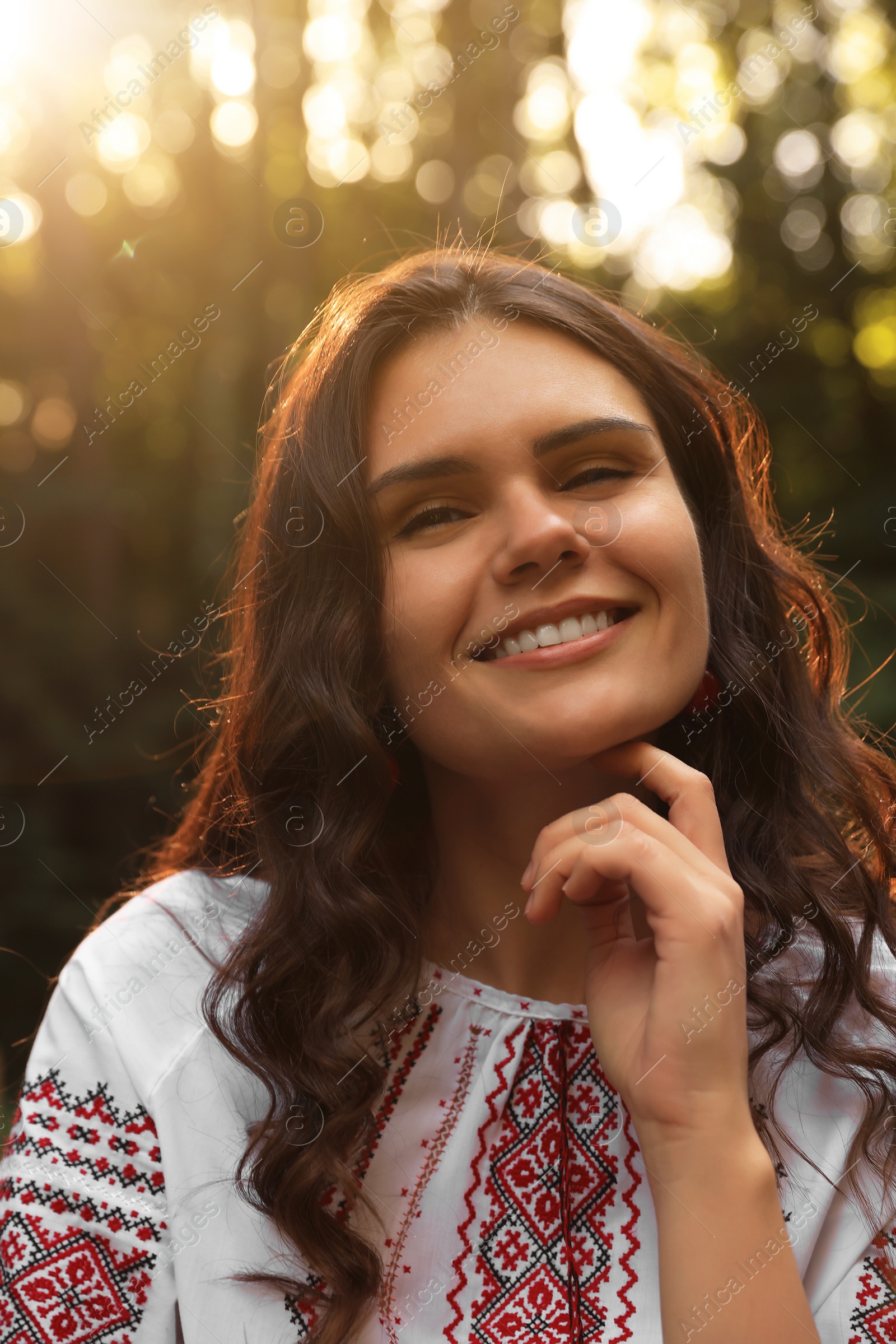 Photo of Beautiful woman in embroidered shirt outdoors on sunny day. Ukrainian national clothes