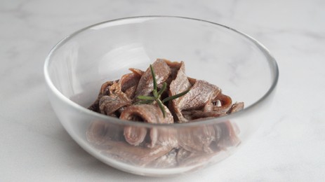 Photo of Canned anchovy fillets in glass bowl on white marble table, closeup