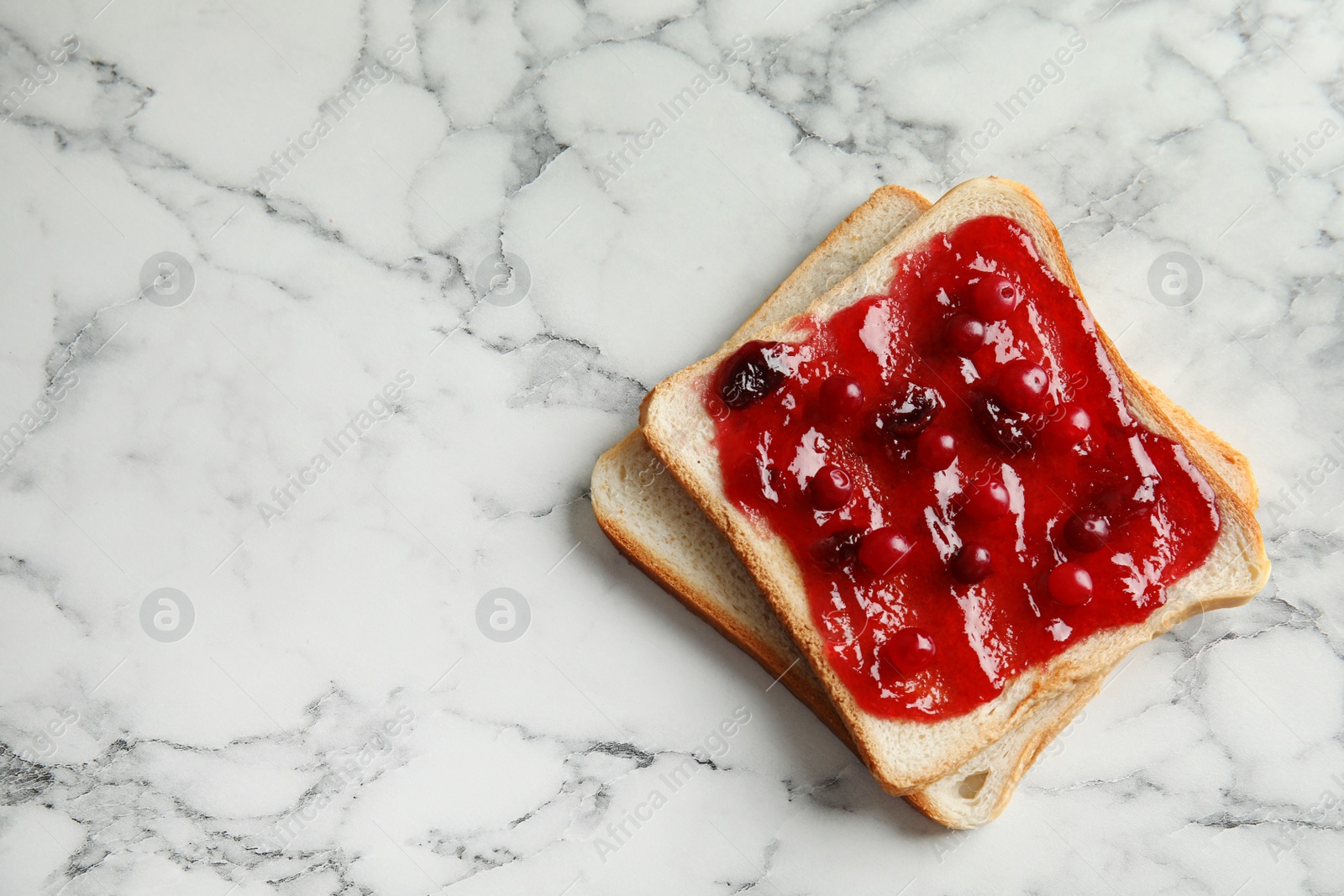 Photo of Slice of bread with jam on white marble table, top view. Space for text