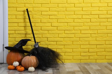 Pumpkins and broom near yellow brick wall in hallway, space for text. Creative Halloween decor