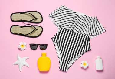 Flat lay composition with striped swimsuit and beach accessories on pink background