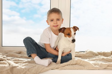 Photo of Little boy with his cute dog on windowsill at home. Adorable pet