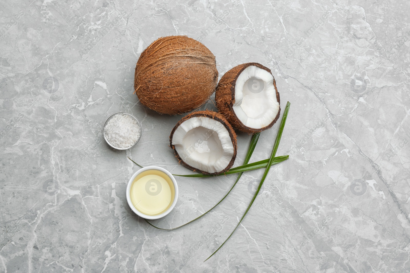 Photo of Bowl of natural organic oil and coconuts on grey stone background, flat lay