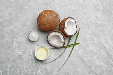 Photo of Bowl of natural organic oil and coconuts on grey stone background, flat lay