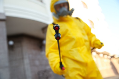 Photo of Person in hazmat suit disinfecting street, focus on sprayer. Surface treatment during coronavirus pandemic