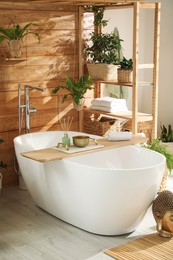 Stylish bathroom interior with white tub and green houseplants near wooden wall. Idea for design