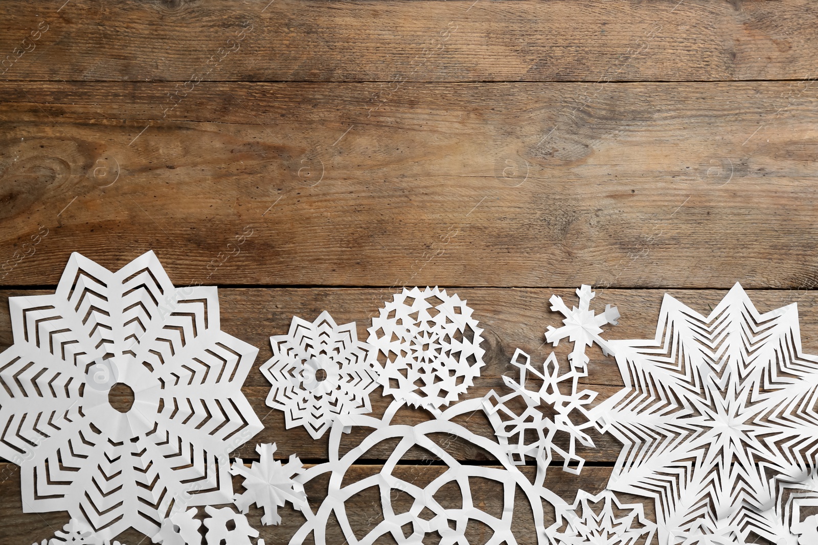 Photo of Many paper snowflakes on wooden background, flat lay. Space for text