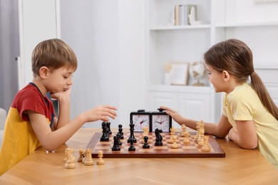 Photo of Cute children playing chess at table in room