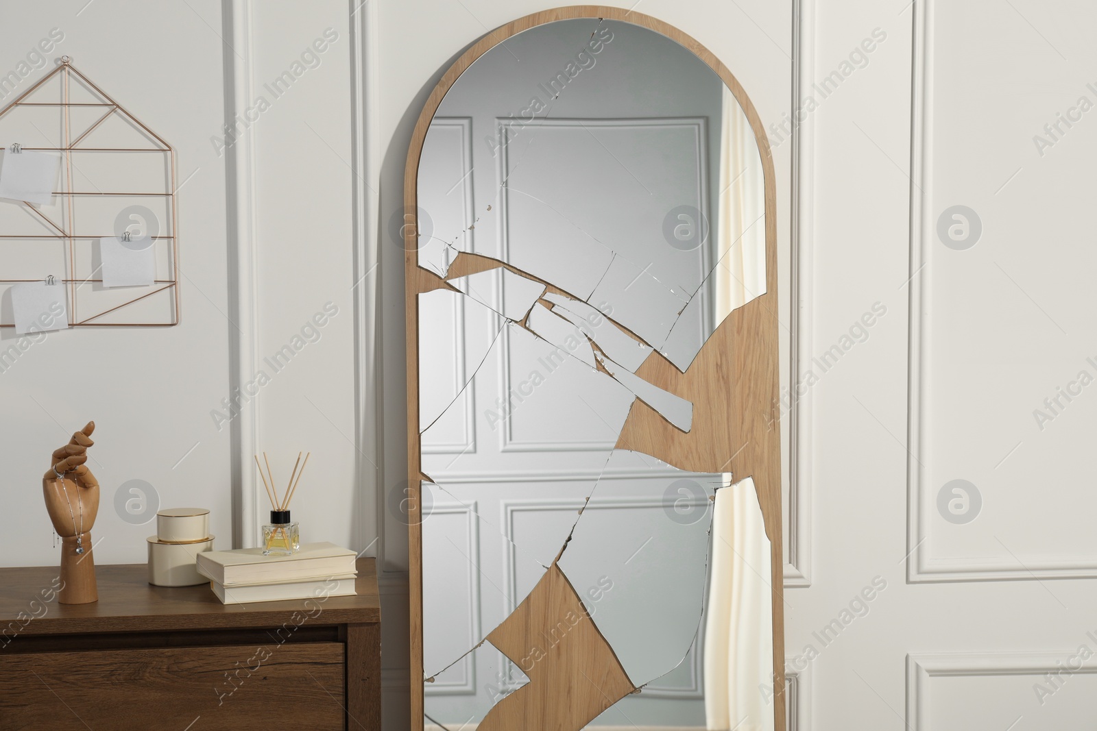 Photo of Broken mirror, reed diffuser and books on wooden chest of drawers in room