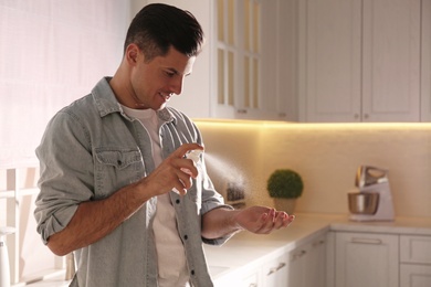 Photo of Man applying spray sanitizer onto hand in kitchen