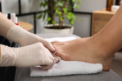 Photo of Pedicurist cutting client`s toenails with scissors in beauty salon, closeup