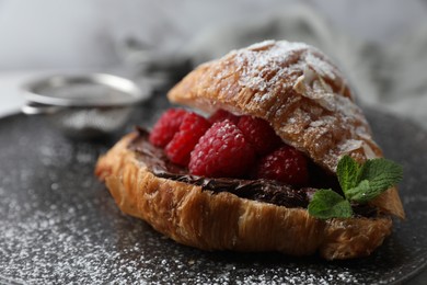 Delicious croissant with raspberries, chocolate and powdered sugar on plate, closeup