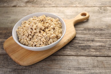 Tasty boiled oatmeal in bowl on wooden table, space for text