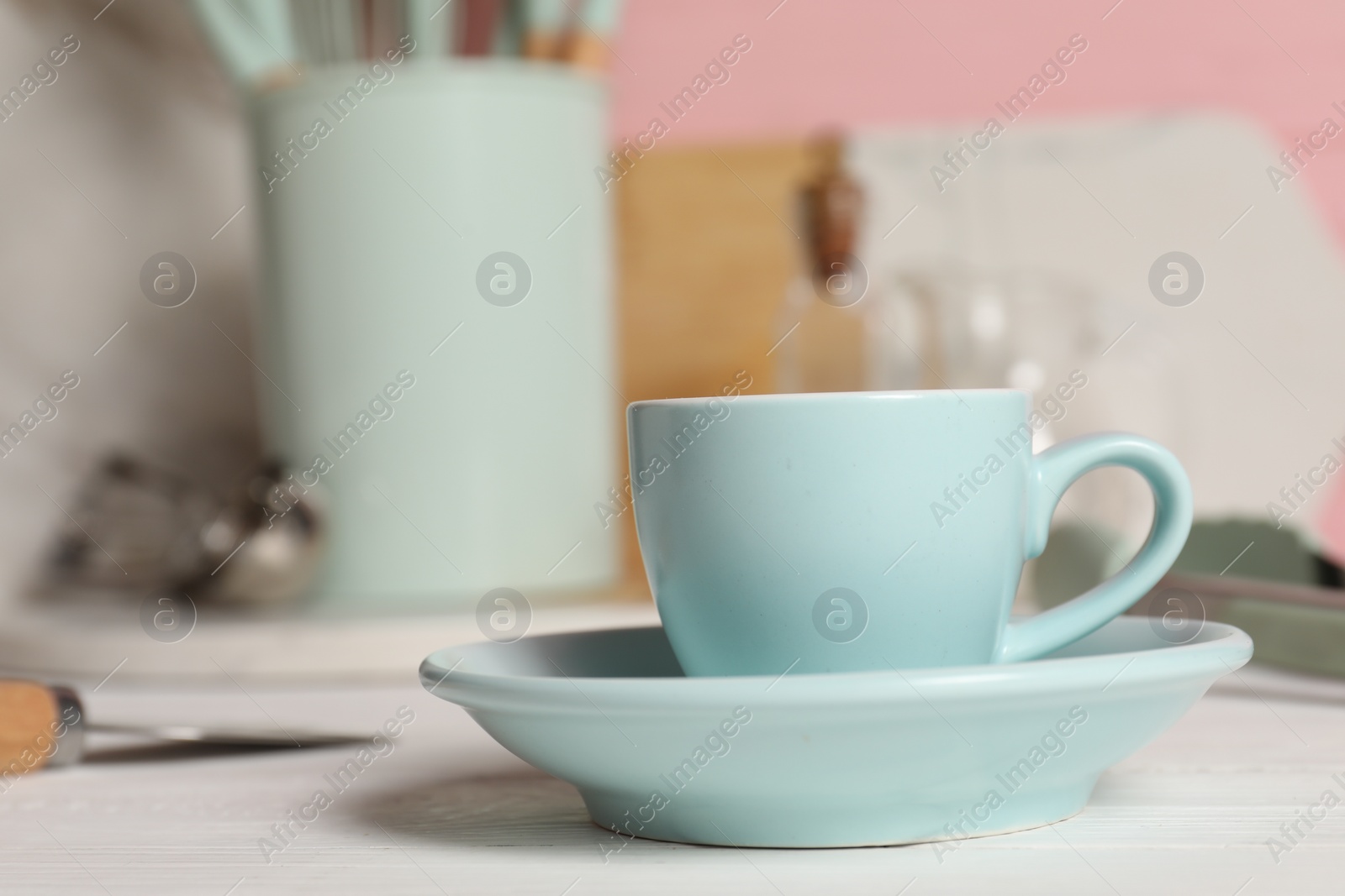 Photo of Light blue ceramic cup with saucer on white wooden table, closeup. Space for text