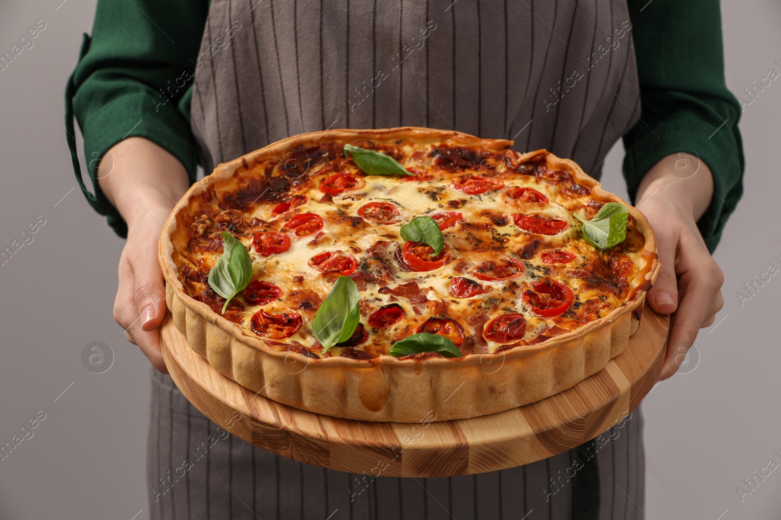 Photo of Woman holding delicious homemade quiche with prosciutto on light grey background, closeup