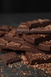 Photo of Pieces and shavings of tasty chocolate on dark table, closeup