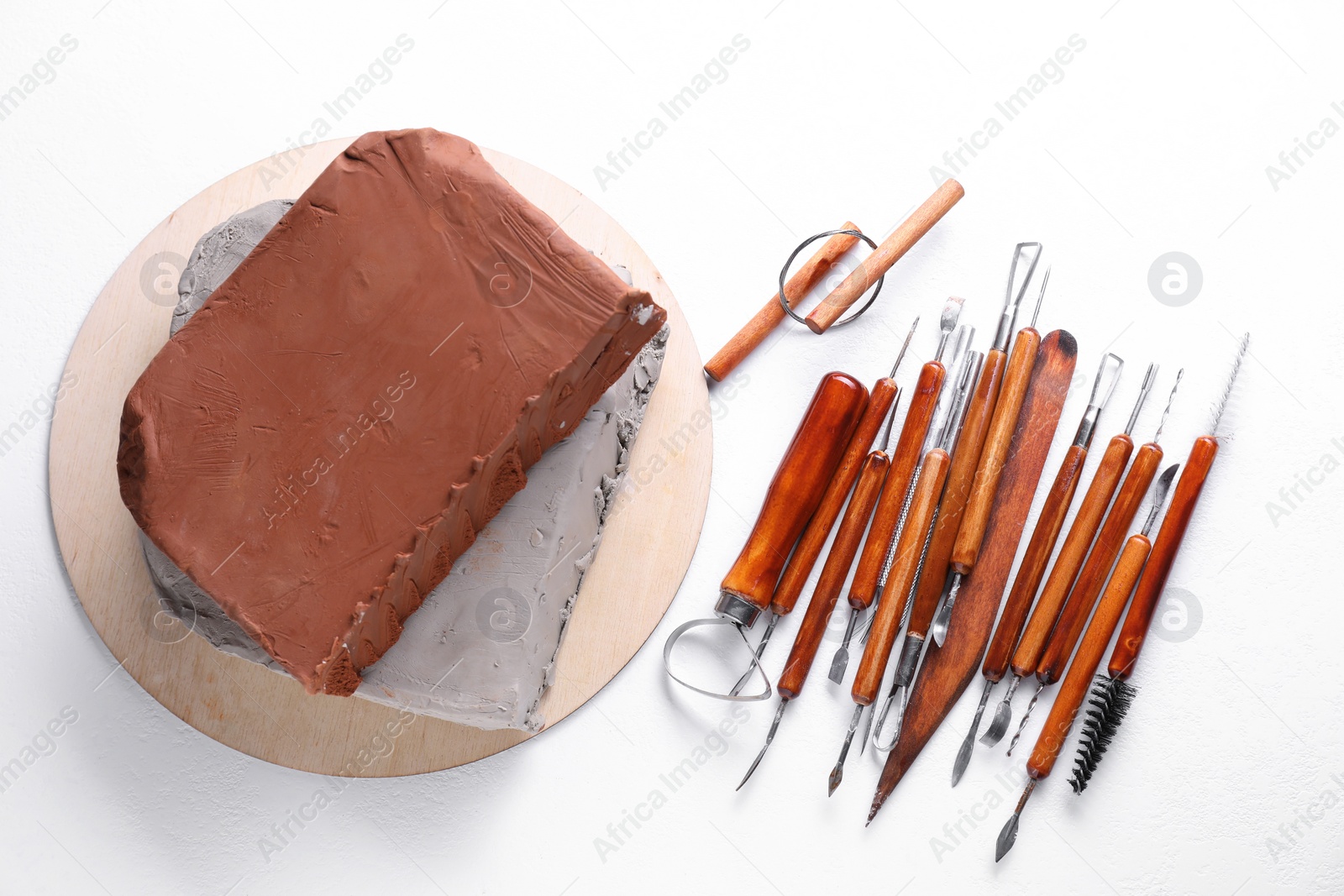 Photo of Clay and set of crafting tools on white textured table, flat lay