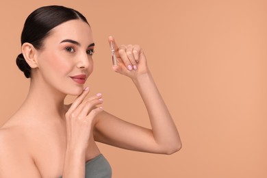 Photo of Beautiful young woman holding skincare ampoule on beige background. Space for text