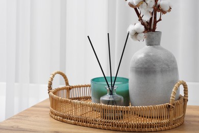 Photo of Candle, reed diffuser and vase with cotton branches on wooden commode indoors
